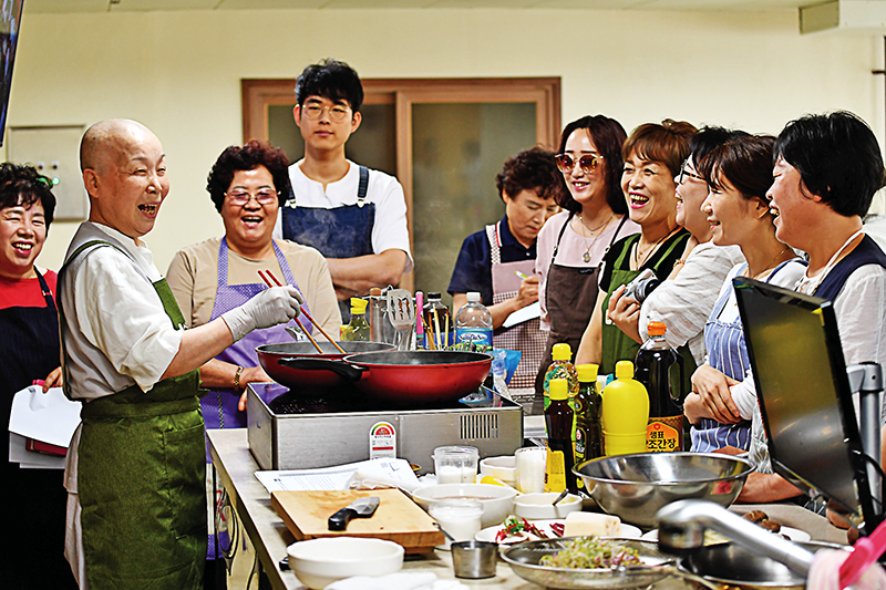 홍승스님이 참가자들과 환하게 웃으며 요리를 선보이고 있다.