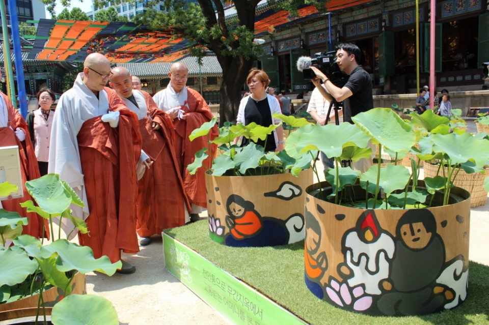 부모은중경의 내용을 표현한 신주욱 작가의 연꽃화분 그림을 보는 스님과 신도들