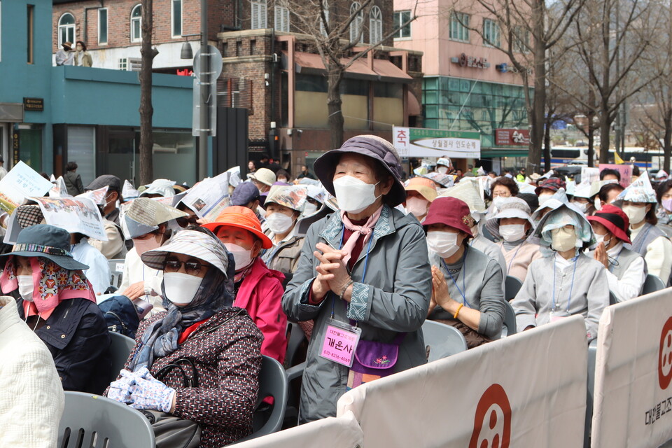 대형 스크린 속 순례단의 모습을 일어서서 보고 있는 신도의 모습이다.