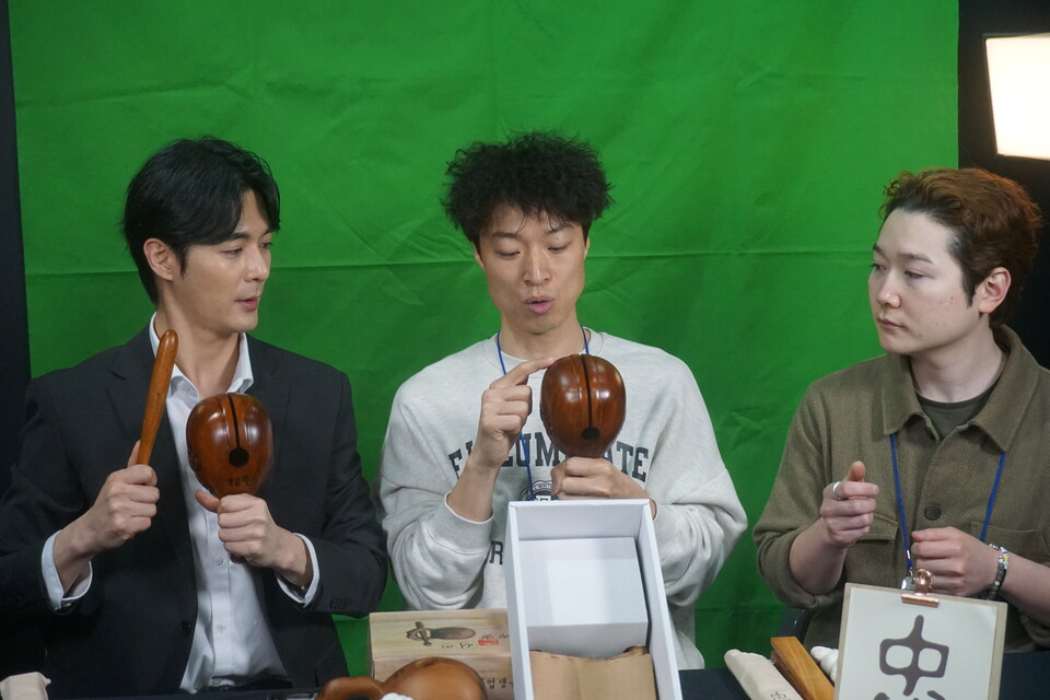 안진석 영천목탁 대표(가운데)가 3월31일 '2023 서울국제불교박람회' 라이브커머스에서 살구나무를 깎아 만든 옻칠 목탁을 들고, 이탁호 쇼호스트(왼쪽)과 강산 불교크리에이터에게 목탁치는 방법을 설명하고 있다.