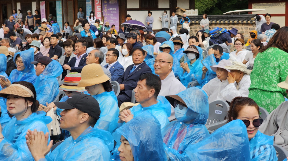갑자기 쏟아진 폭우로 잠시 행사를 멈췄다가 재개할 때, 우비를 입고 청중들이 객석에 들어앉아 있다.